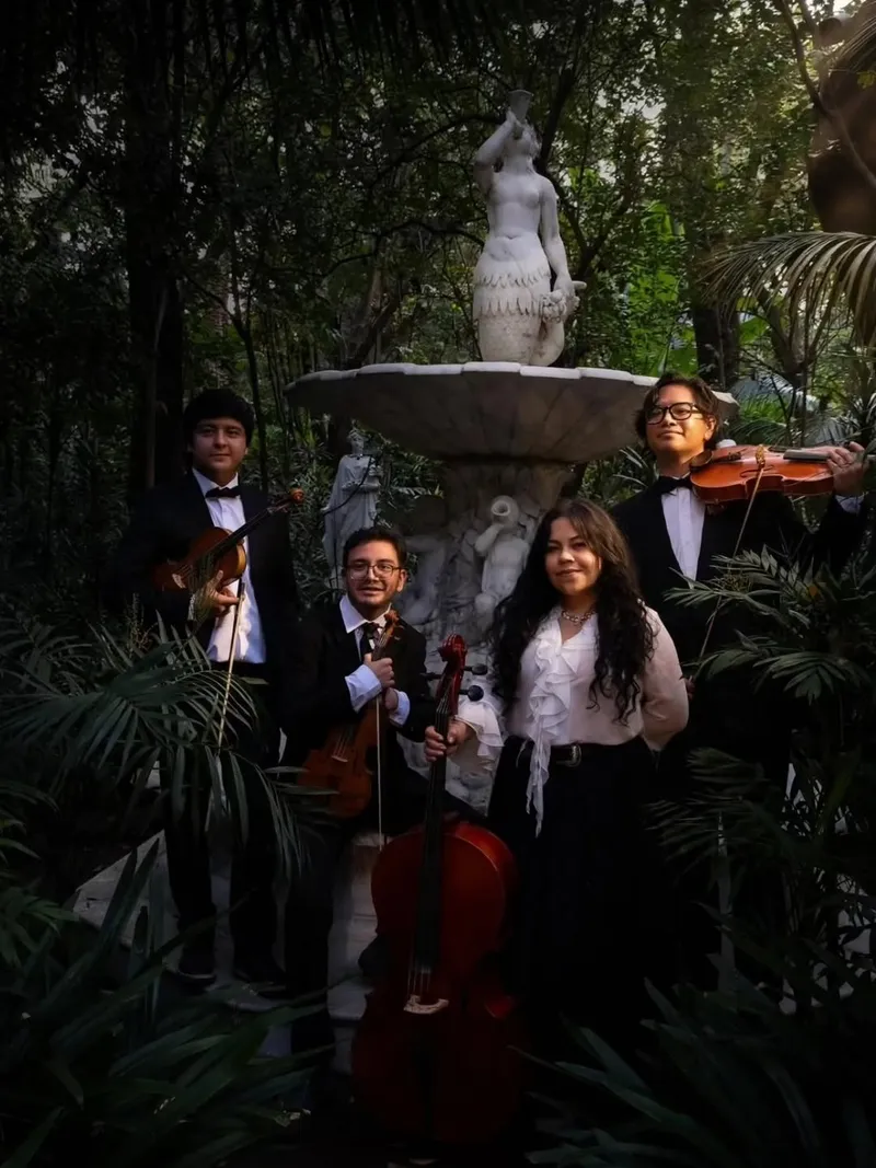 Integrantes del Ensamble Quincunce con sus instrumentos junto a una fuente con escultura