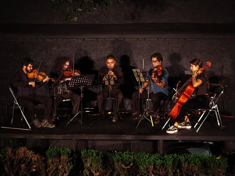 El ensamble tocando sentado en un escenario oscuro con atriles